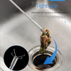 A close-up of a four-claw hand grip drain tool being used to remove a stuck item from a kitchen sink drain.