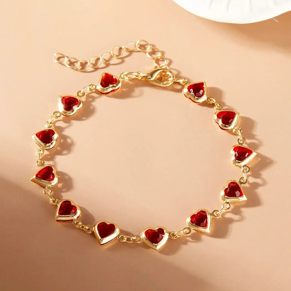 Goldfarbener Armband mit kleinen, facettierten roten Kristallherz-Anhängern.