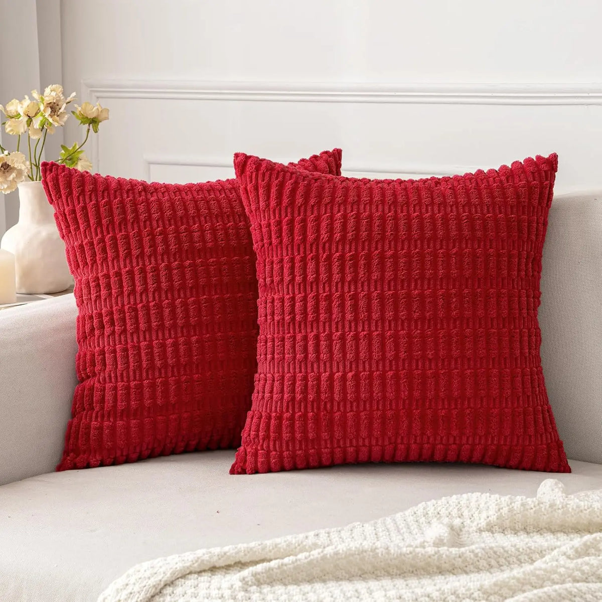 A deep red knitted throw pillow cover with a textured pattern resting on a white sofa.