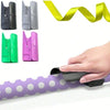 A hand is shown using a portable wrapping paper cutter with a sliding blade to cut a purple polka-dot paper roll.