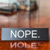 A black aluminum desk sign with white text that reads NOPE.
