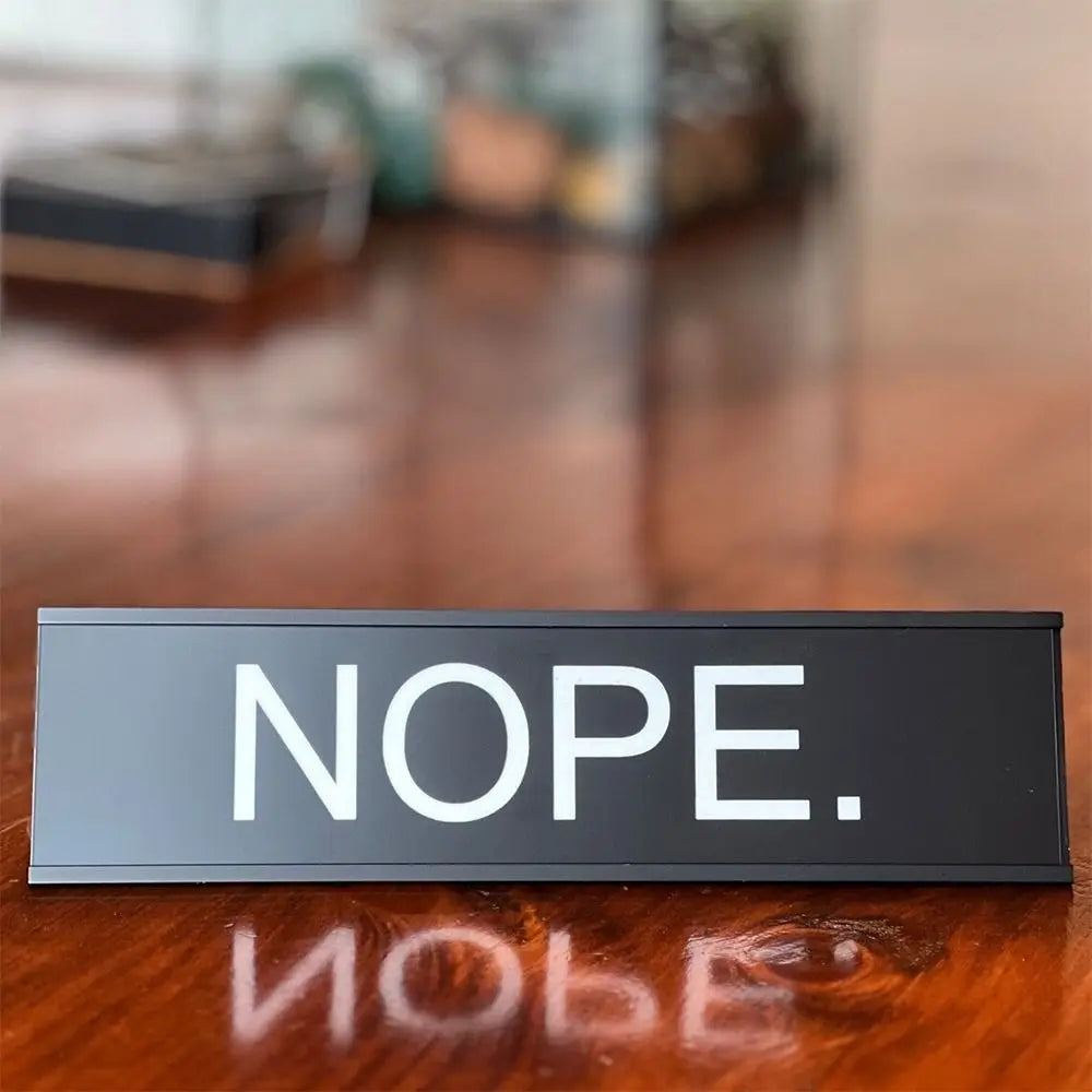 A black aluminum desk sign with white text that reads NOPE.