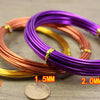 Three coils of anodized aluminum jewelry wire in gold, copper, and purple colors are displayed on a wooden surface.