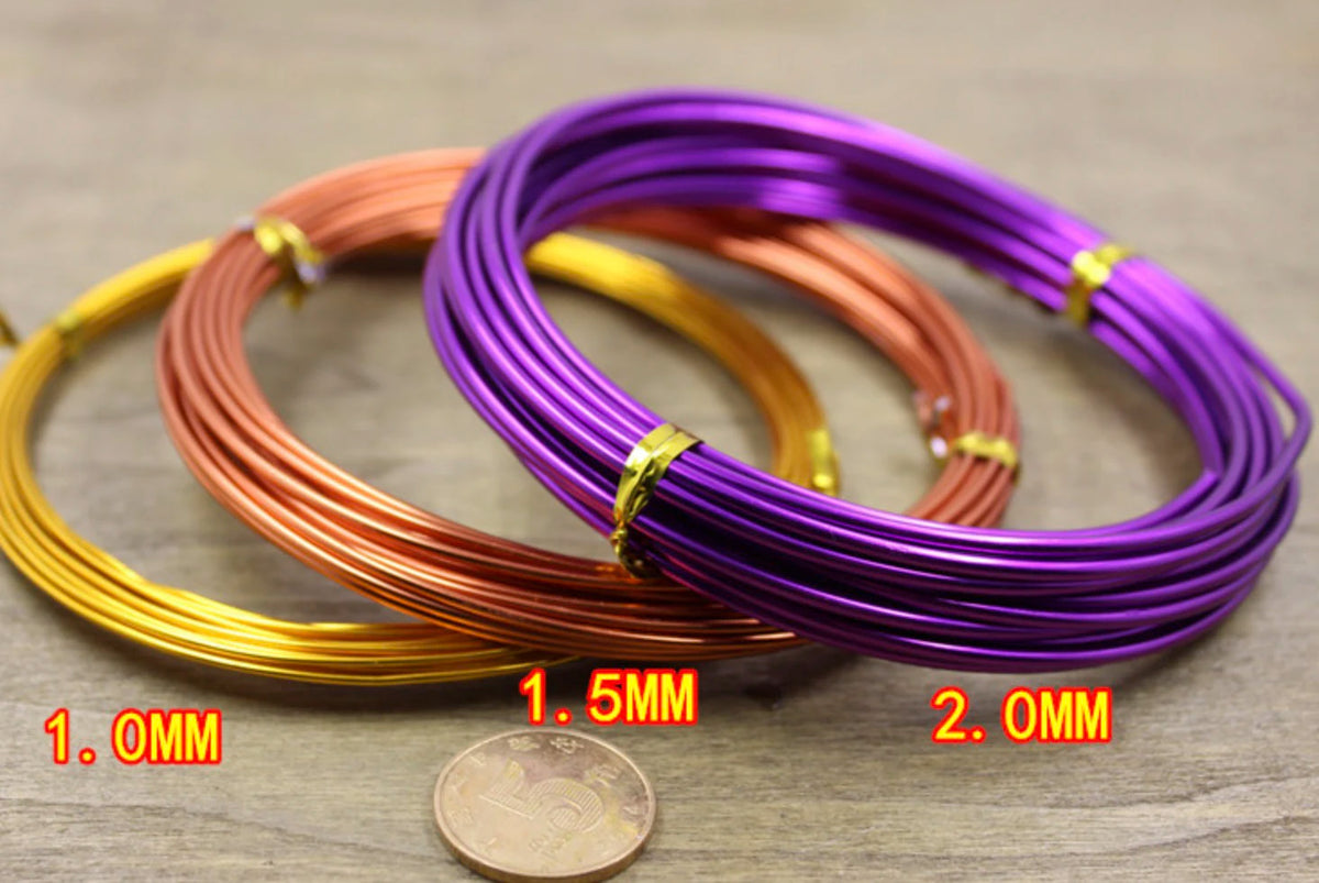 Three coils of anodized aluminum jewelry wire in gold, copper, and purple colors are displayed on a wooden surface.