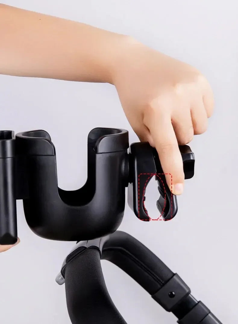 A hand is shown gripping a black 2-in-1 stroller cup holder and phone mount device.