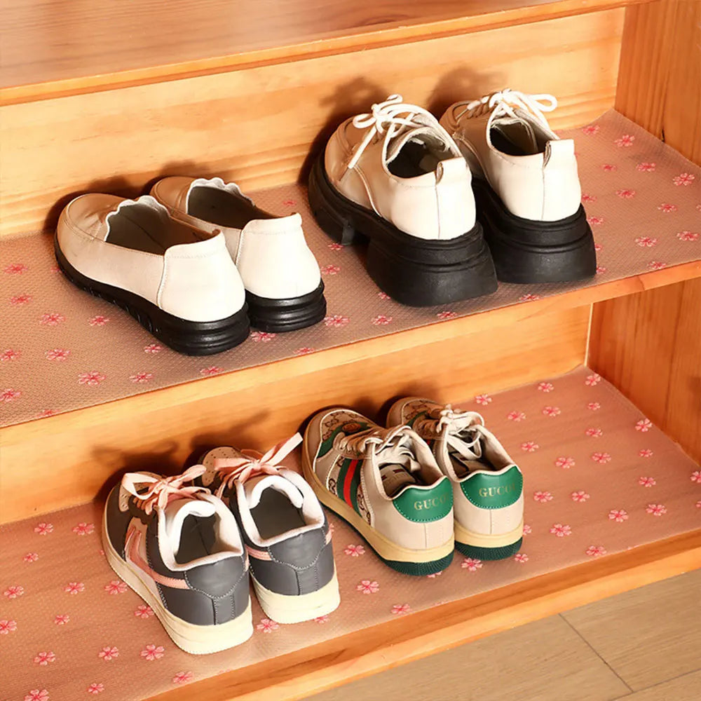 A pair of white leather shoes are displayed on a wooden shelf with pink patterned lining.