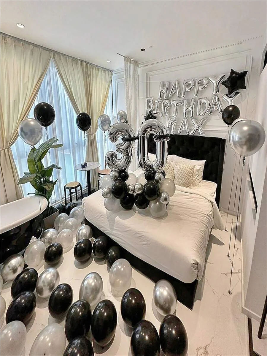 A bedroom decorated for a birthday party with black and silver balloons and foil numbers