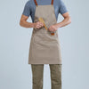 A man wearing a beige waterproof kitchen apron over a gray shirt and olive green pants.
