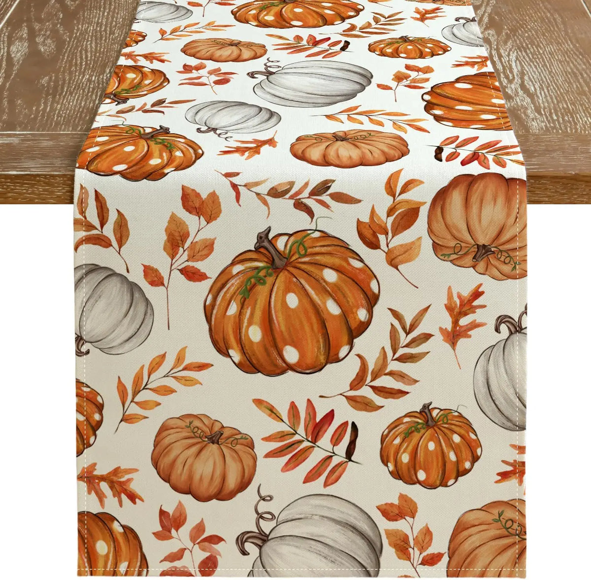 Linen table runner featuring an orange and white fall pumpkin and maple leaf pattern on a cream background.