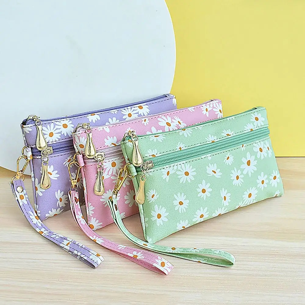 A collection of five daisy print PU leather wristlet wallets in purple, pink, and green are displayed on a light wooden surfa