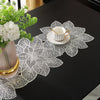 A set of ornate white lace table runners and placemats with floral designs placed on a black table.