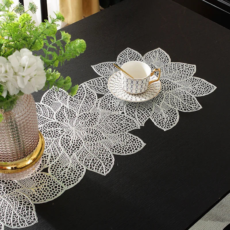 A set of ornate white lace table runners and placemats with floral designs placed on a black table.