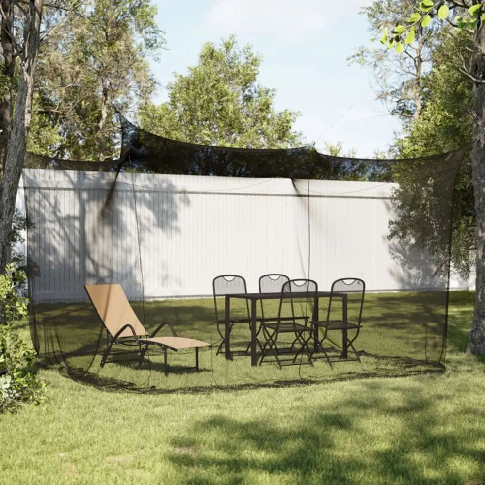 A large mesh fly net canopy is set up over a patio area with a table and chairs, surrounded by trees.