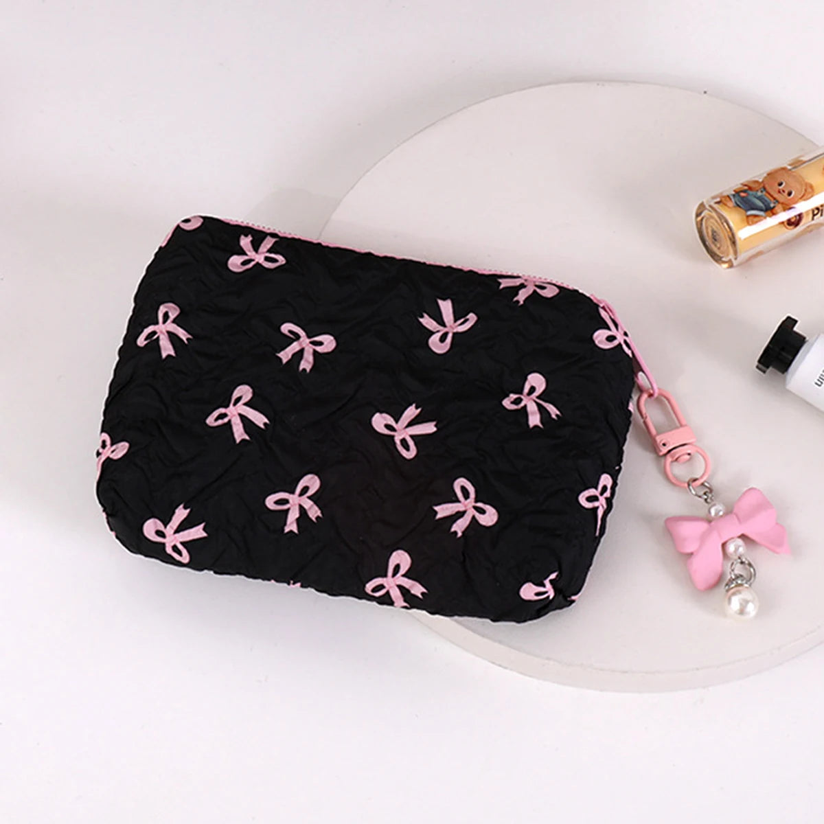 A black quilted makeup bag decorated with pink bows is shown on a white surface.