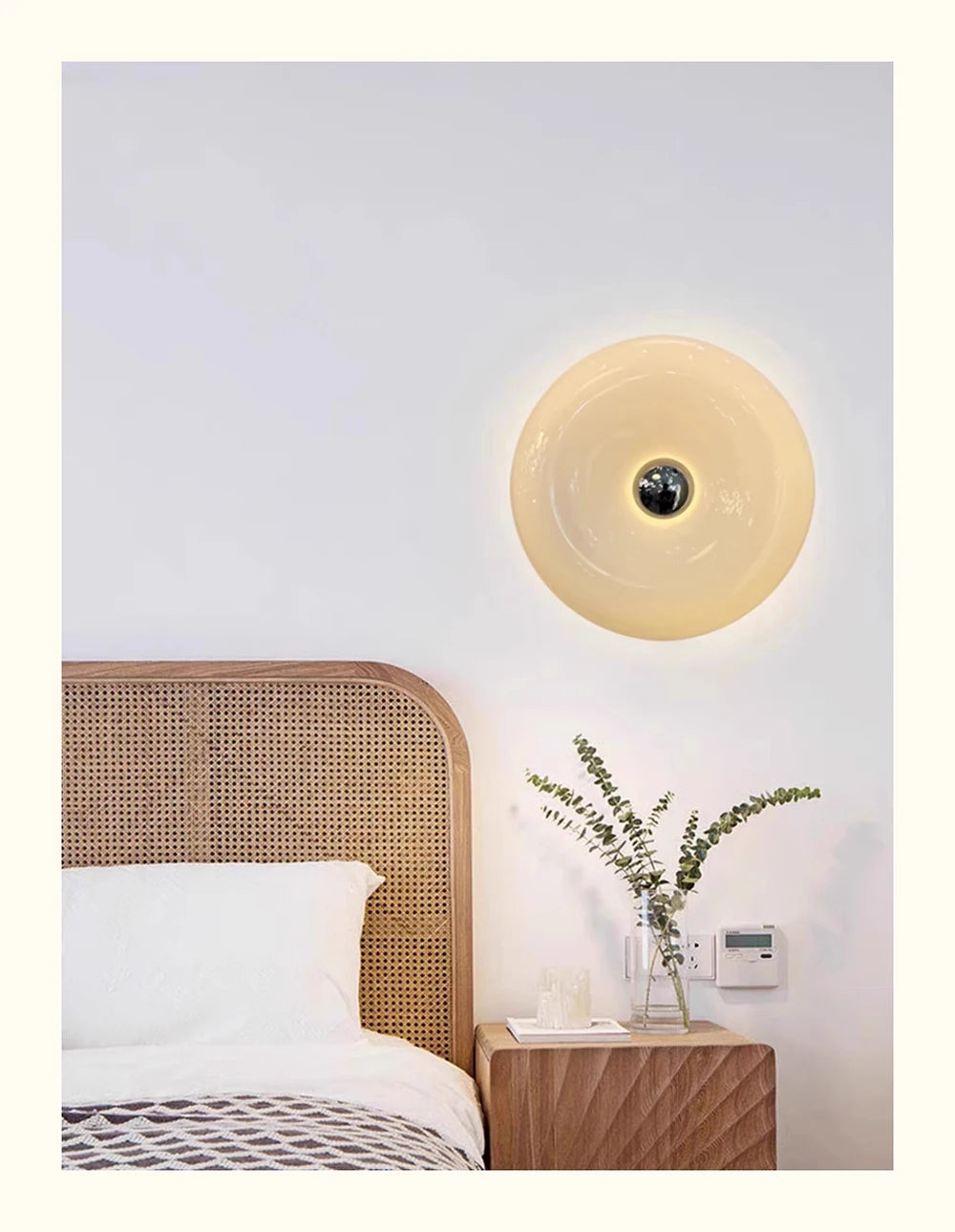 A modern, round, translucent yellow LED wall sconce with a touch dimming feature mounted on a white wall above a wooden bed.