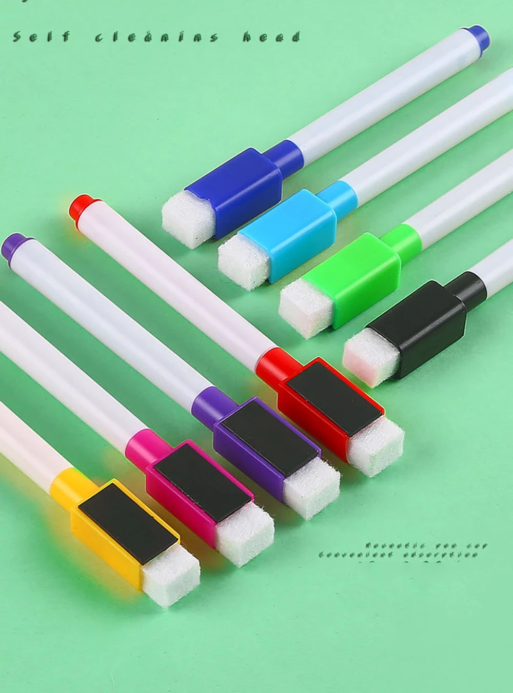 Eight fine tip whiteboard markers in assorted colors and white tips are arranged on a green surface.