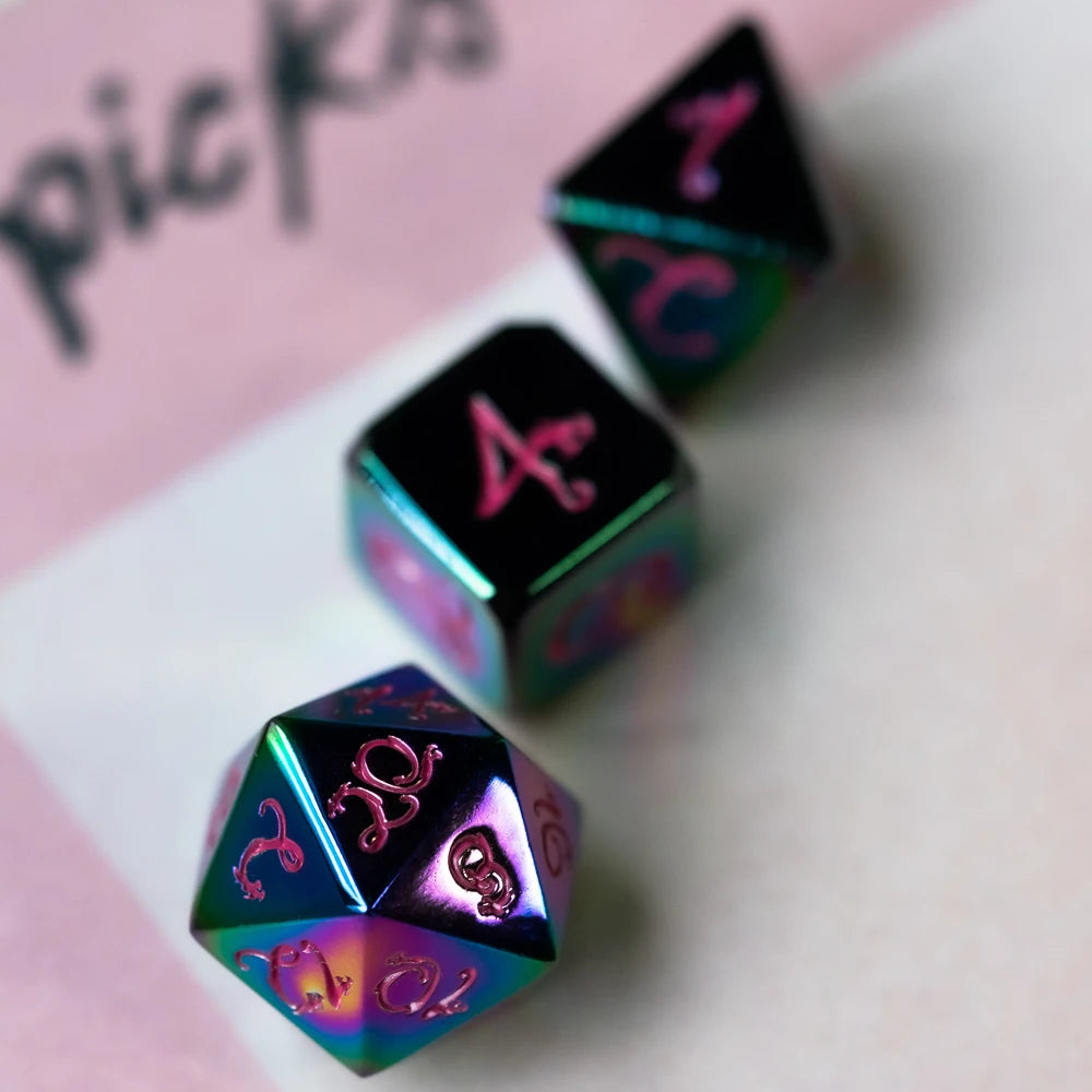 A close-up of several metal polyhedral dice with a dragon font design scattered on a white surface.