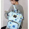 A woman is holding a light blue waterproof diaper bag backpack with blue floral and cloud patterns.
