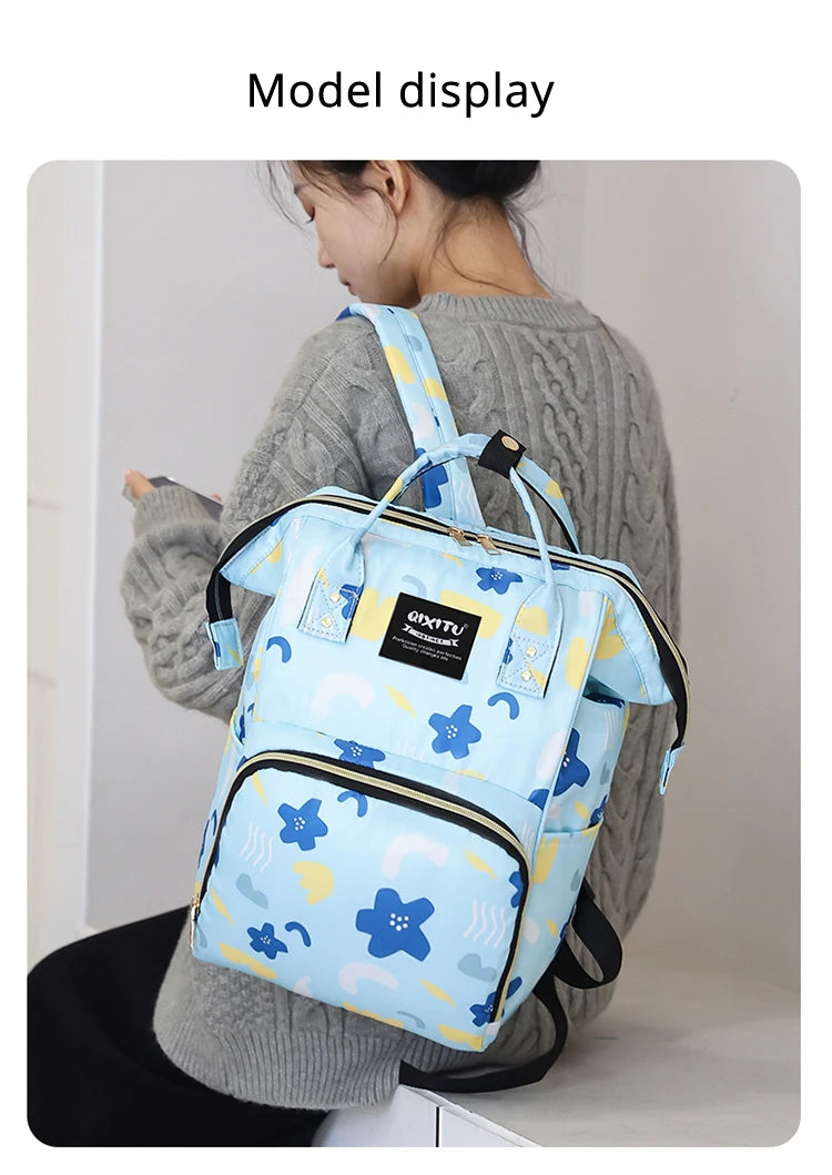 A woman is holding a light blue waterproof diaper bag backpack with blue floral and cloud patterns.