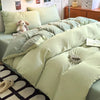 A light sage green duvet cover set with a matching pillow and a stuffed animal on a bed.