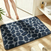 A dark blue plush non-slip bathroom rug with a pebble texture placed on a light wooden floor.
