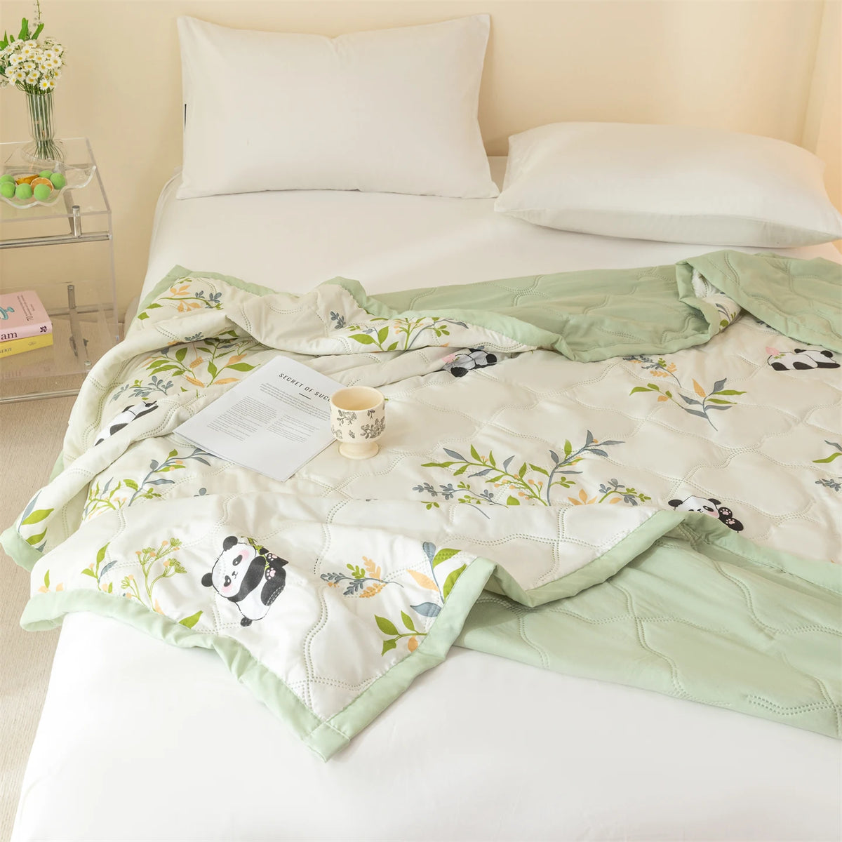 A light green quilted summer quilt featuring a white background and cute panda patterns is displayed on a white bed.