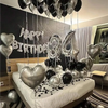 A silver and black balloon garland featuring oversized foil numbers decorating a bed for a birthday celebration.