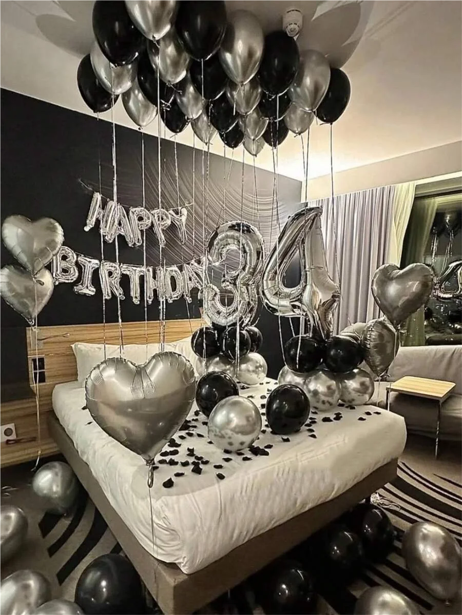 A silver and black balloon garland featuring oversized foil numbers decorating a bed for a birthday celebration.