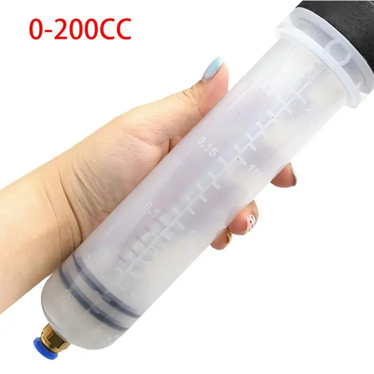 A hand is holding a clear manual fluid transfer syringe pump with measurement markings for oil or brake fluid extraction.