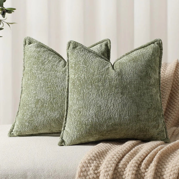 A textured sage green chenille throw pillow resting on a beige fabric surface.