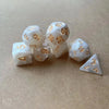 A set of seven white pearl pattern polyhedral dice arranged diagonally on a light brown surface.