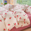 A set of pink bedding featuring a duvet cover and pillows with a pattern of red cherries on a cream background.