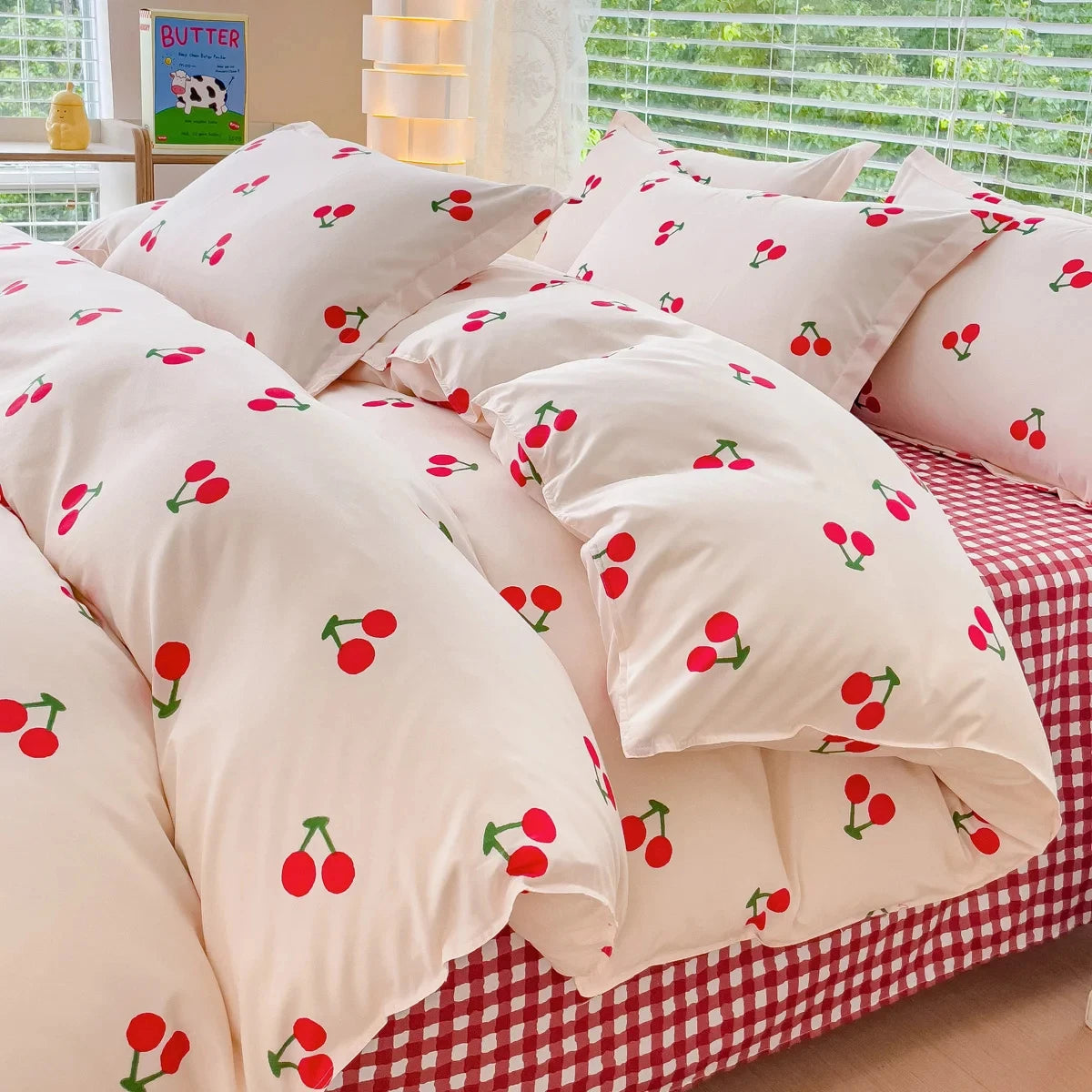 A set of pink bedding featuring a duvet cover and pillows with a pattern of red cherries on a cream background.
