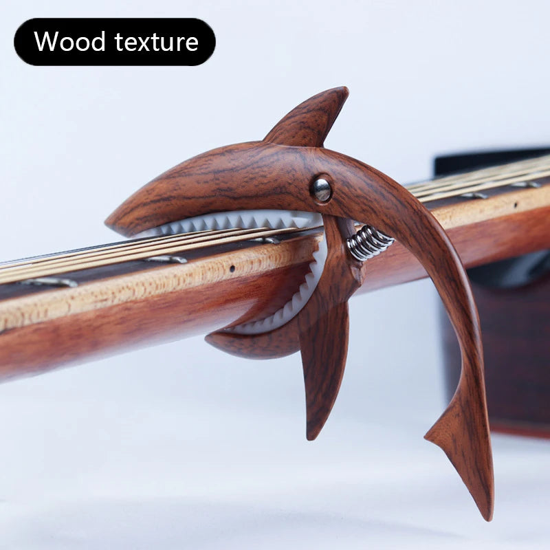 A close-up of a wooden guitar capo with a shark-like design and zinc alloy build.