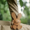 A small, light brown bunny-shaped bag charm keychain is visible against a soft beige fabric background.