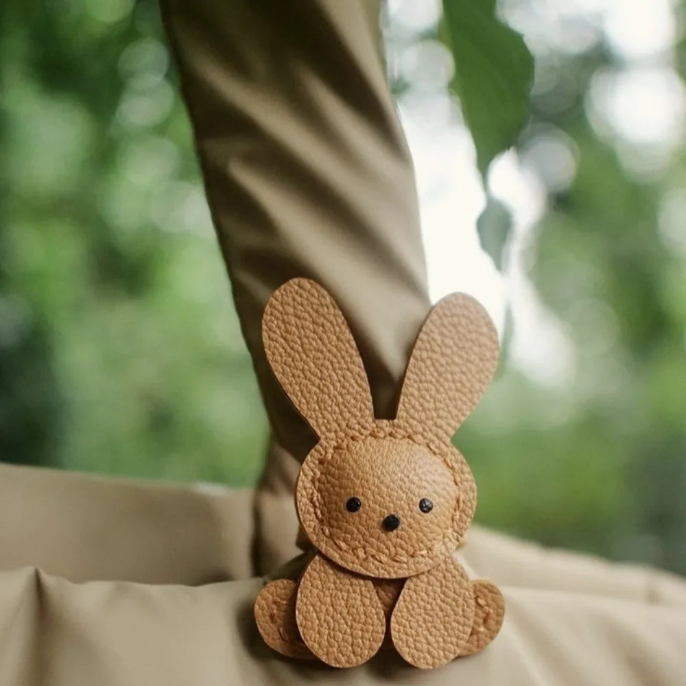 A small, light brown bunny-shaped bag charm keychain is visible against a soft beige fabric background.