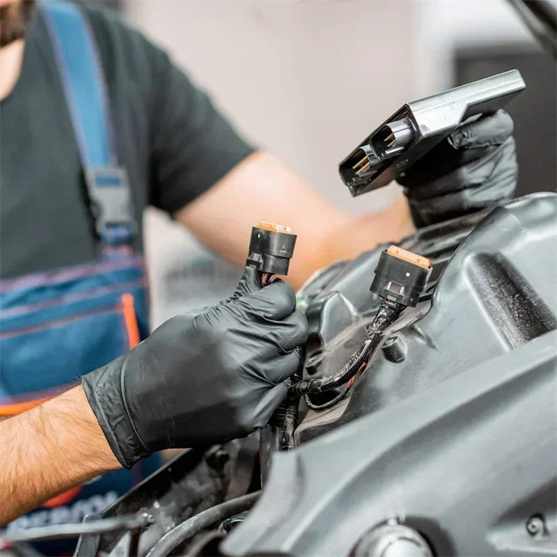 A person wearing black nitrile disposable gloves is using a tool to work on a car engine component.
