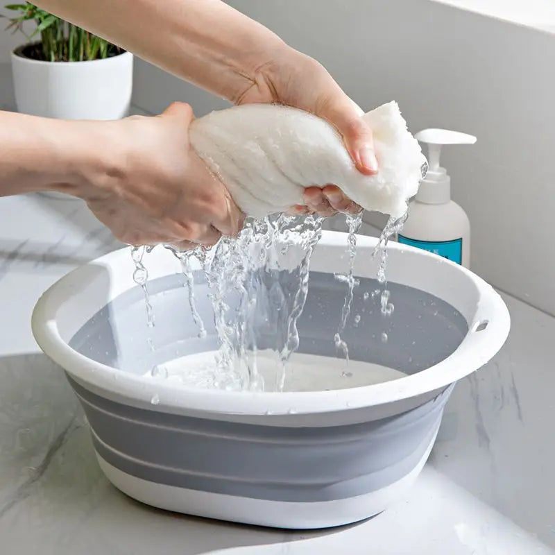 A hand is pouring water over a white, fluffy cloth inside a gray plastic wash basin.