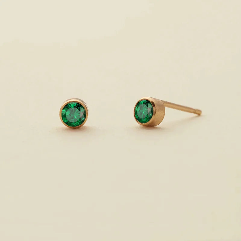 Une paire de clous dorés minimalistes avec des pierres de naissance vert vif.