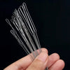 A hand holds a set of seven ultra-fine beading needles for jewelry making against a dark background.