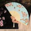 A hand holds an open bamboo and silk folding fan with a light blue background and pink floral design.