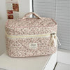 A pink floral quilted cosmetic bag with a light yellow lining and fabric ribbon, resting on a white surface.