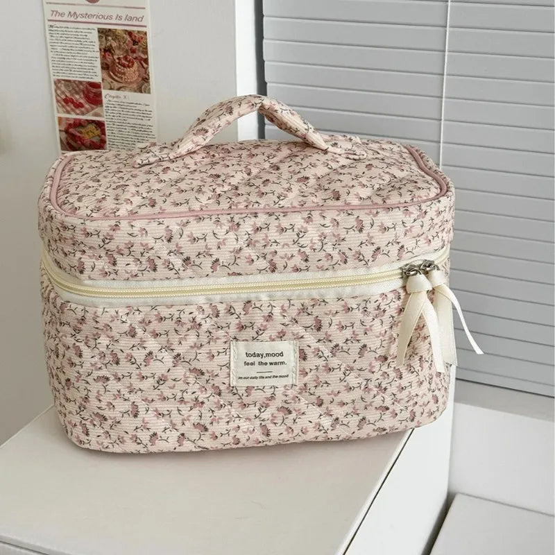 A pink floral quilted cosmetic bag with a light yellow lining and fabric ribbon, resting on a white surface.