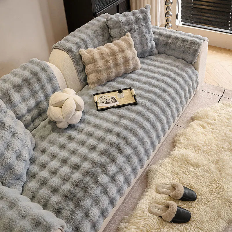 A gray plush sofa cushion cover with textured fabric and decorative pillows on a light-colored sofa.
