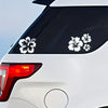 A close-up of a white car's rear window featuring black hibiscus flower decals.