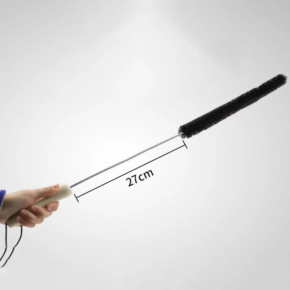 Une main tient une longue brosse de nettoyage noire avec un manche métallique et une longueur de 27 cm sur un fond gris clair