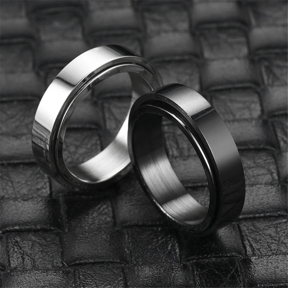 A pair of shiny stainless steel anxiety spinner rings resting on a dark leather surface.