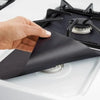 A hand places a black reusable gas stove burner protector onto a stovetop grate.