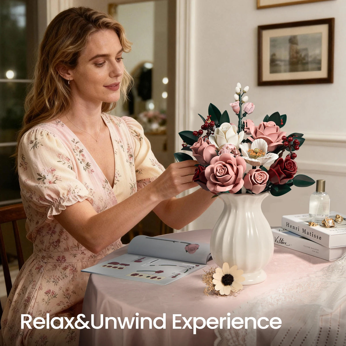 A woman is arranging a pink rose bouquet on a table with a small box and a framed picture.