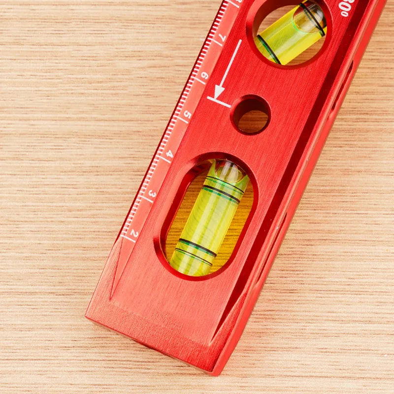 A red magnetic aluminum level ruler with V-grooves for precise angle measurement is shown on a wooden surface.